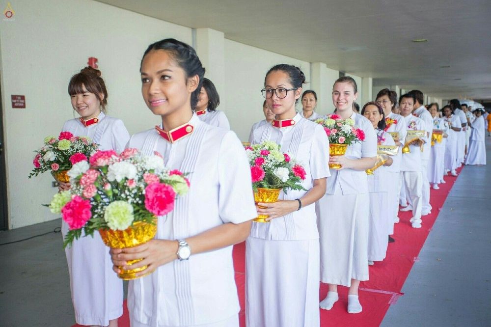 กลุ่มคนในชุดขาวถือพานดอกไม้เดินเรียงแถวบนพรมแดงในพิธีทางศาสนา