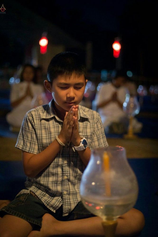 เด็กชายพนมมือสวดมนต์ในบรรยากาศงานบุญกฐินยามค่ำคืนที่ศูนย์ปฏิบัติธรรม