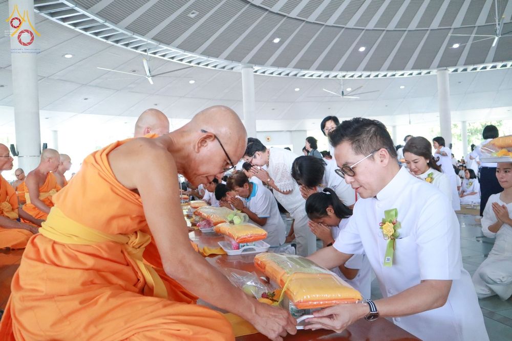 พุทธศาสนิกชนชายสวมชุดขาวกำลังประเคนไทยธรรมแด่พระภิกษุสงฆ์ในพิธีบุพเปตพลี ณ หอฉันคุณยายอาจารย์มหารัตนอุบาสิกาจันทร์ ขนนกยูง วัดพระธรรมกาย