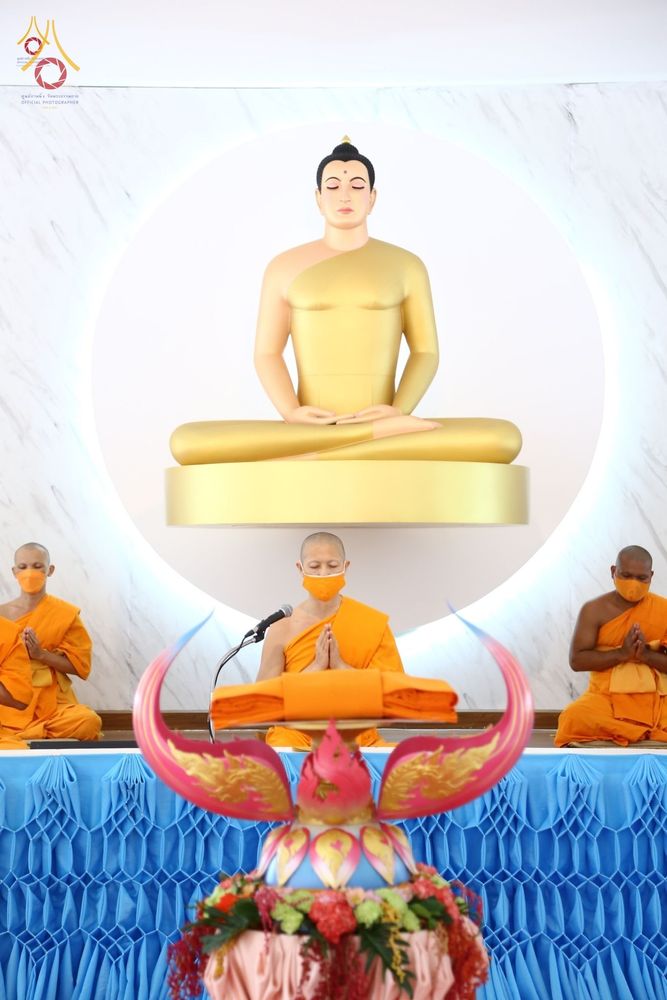 พระสงฆ์สามรูปนั่งประกอบพิธีทางศาสนาเบื้องหน้าพระพุทธรูปปางสมาธิสีทอง