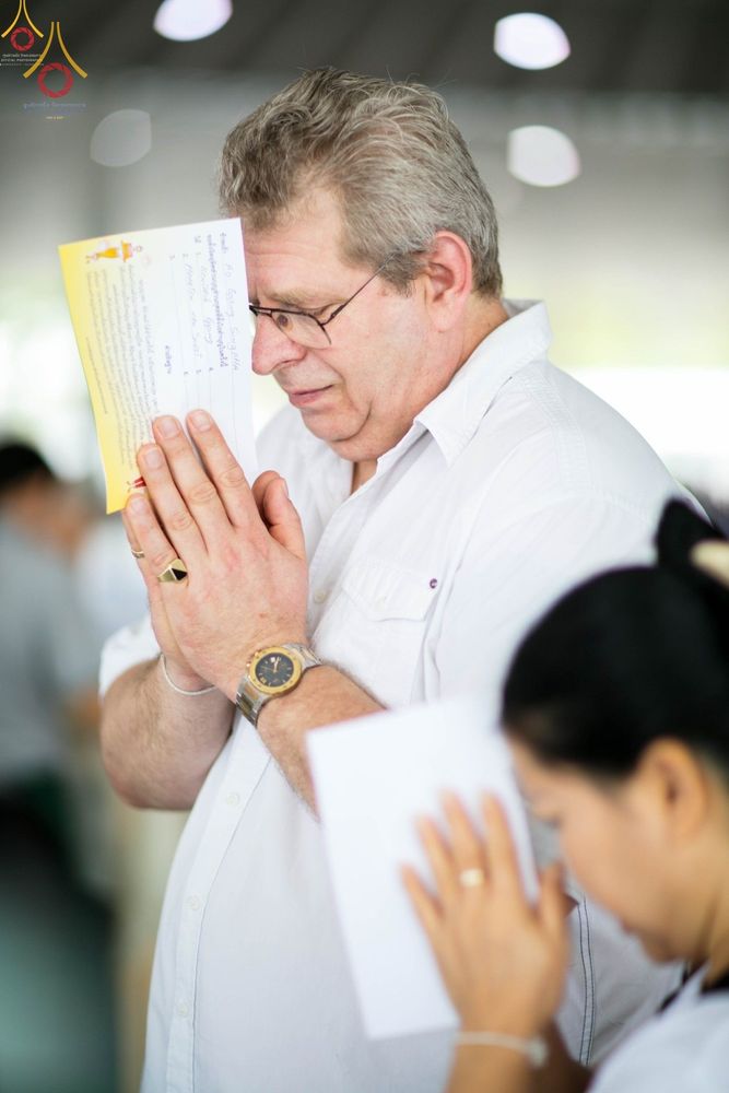 ชายชาวต่างชาติพนมมือถือแผ่นกระดาษบทสวดในพิธีปุพพเปตพลีที่วัดพระธรรมกาย