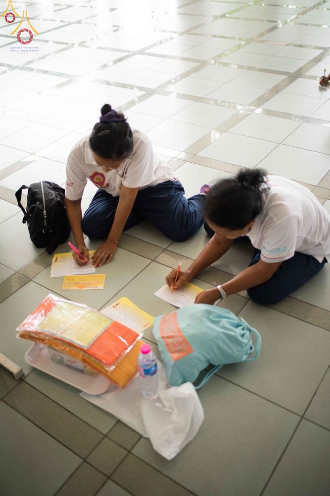 สาธุชนหญิงสองท่านนั่งเขียนเอกสารอุทิศส่วนกุศลบนพื้นกระเบื้องภายในหอฉันคุณยายอาจารย์ฯ วัดพระธรรมกาย