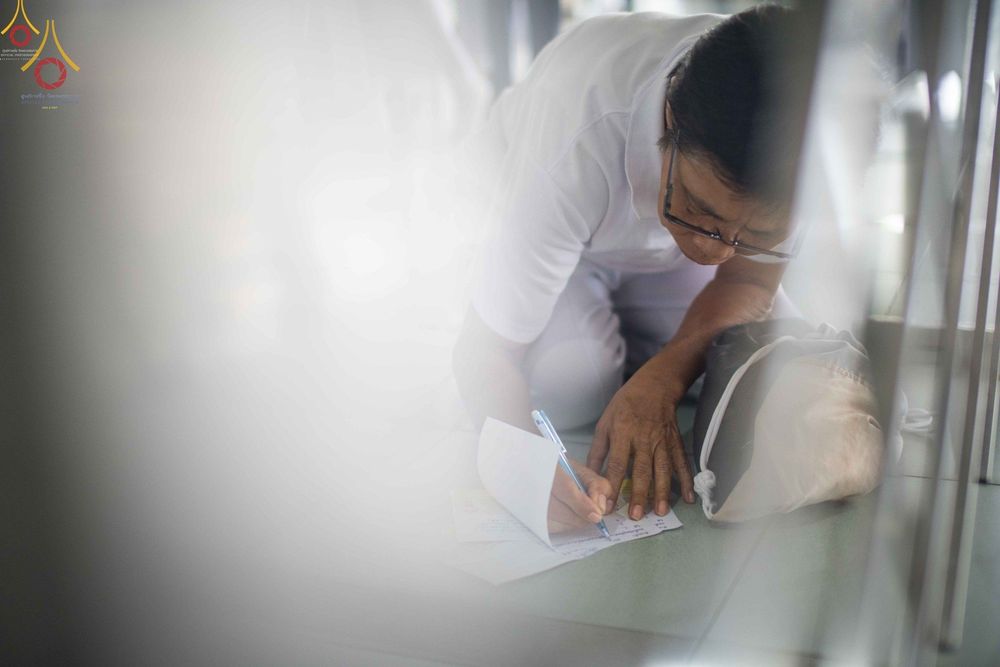 พุทธศาสนิกชนสวมชุดขาวกำลังก้มลงเขียนชื่อบนกระดาษเพื่ออุทิศส่วนกุศลให้แก่หมู่ญาติที่ล่วงลับ ในพิธีปุพพเปตพลี ณ หอฉันคุณยายอาจารย์ฯ วัดพระธรรมกาย