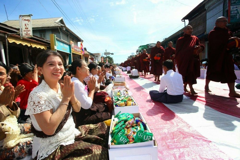 พุทธศาสนิกชนนั่งพนมมือรอตักบาตรพระสงฆ์จำนวนมากที่เดินรับบิณฑบาตบนถนนในเมืองทวาย