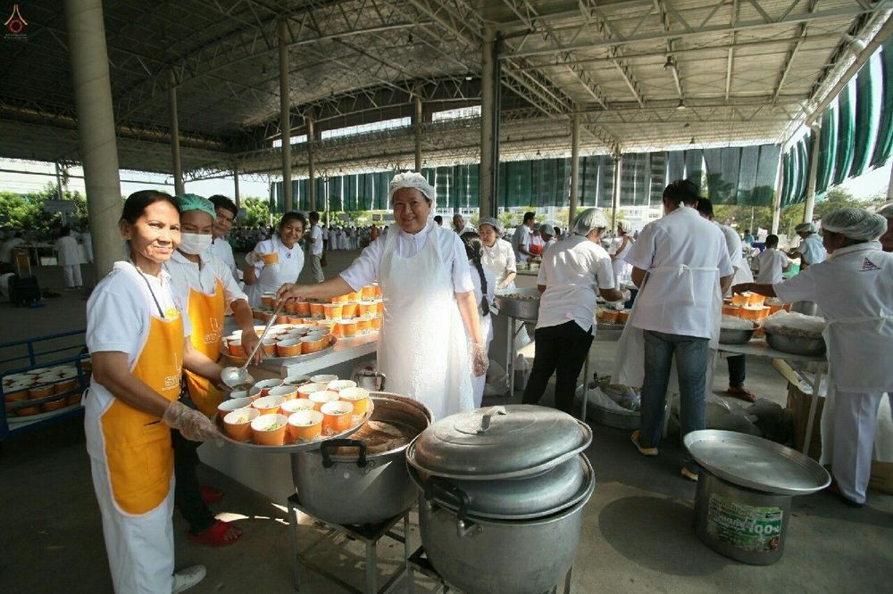 อาสาสมัครสวมชุดขาวและผ้ากันเปื้อนกำลังตักอาหารใส่ถ้วยในโรงทาน