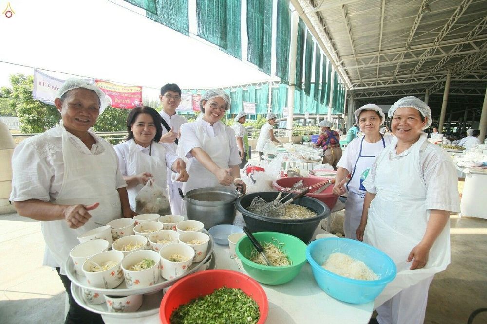 กลุ่มอาสาสมัครสวมชุดขาวกำลังช่วยกันจัดเตรียมอาหารใส่ถ้วยในโรงทาน