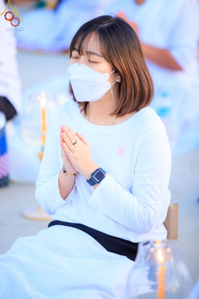 หญิงสาวสวมชุดขาวนั่งพนมมือหลับตาด้วยความสงบในพิธีจุดประทีปถวายเป็นพุทธบูชา