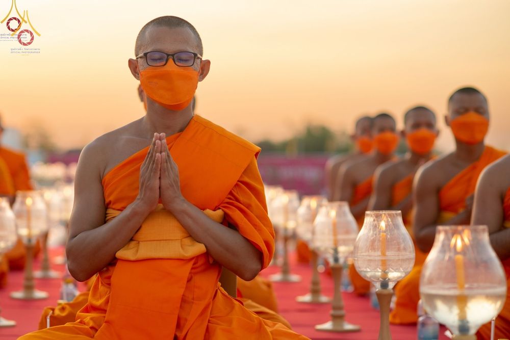 พระภิกษุสงฆ์ในจีวรสีส้มพนมมือทำสมาธิท่ามกลางโคมประทีปในพิธีทางศาสนา