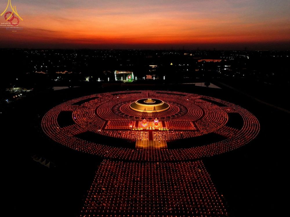 ภาพมุมสูงของพุทธศาสนิกชนจุดประทีปจำนวนมากเป็นวงกลมล้อมรอบอนุสรณ์สถานในช่วงเวลาโพล้เพล้