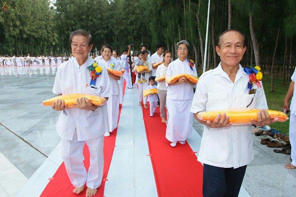 กลุ่มพุทธศาสนิกชนแต่งกายชุดขาวถือผ้าไตรจีวรสีเหลืองทองเดินบนพรมแดงในพิธีทอดกฐิน