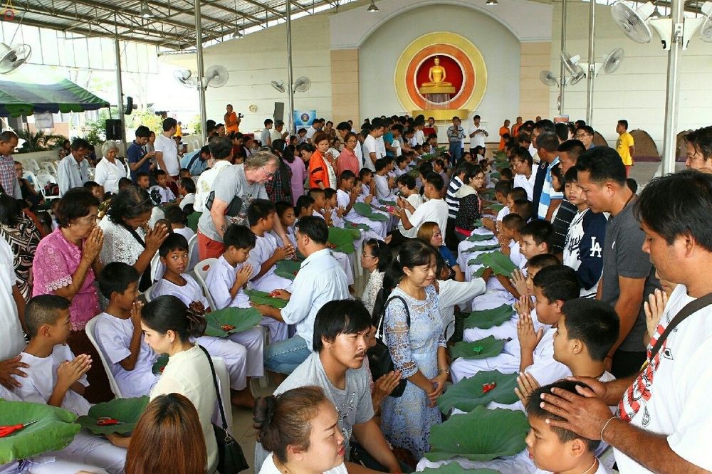 กลุ่มนาคในชุดขาวนั่งรอพิธีปลงผมโดยมีญาติมิตรล้อมรอบในอาคาร