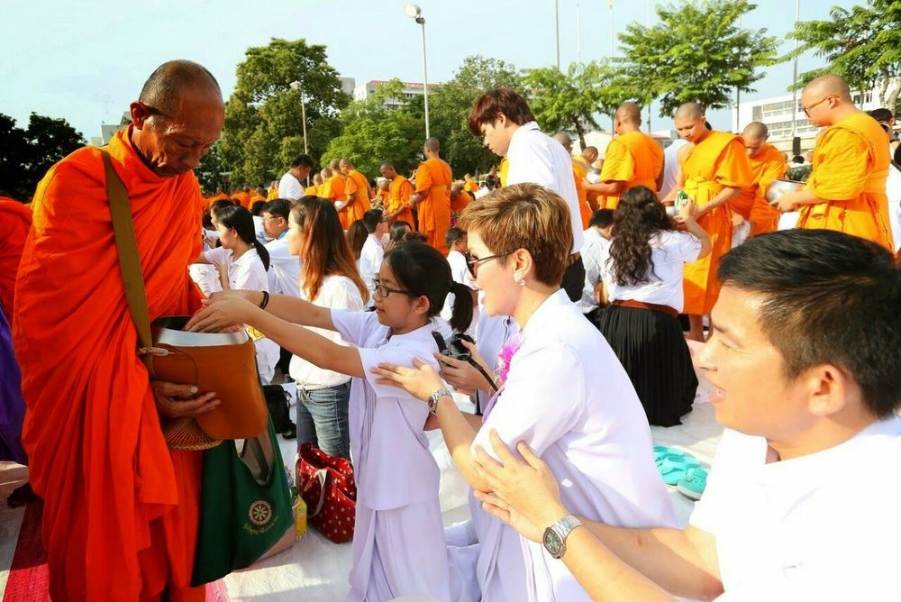 พุทธศาสนิกชนสวมชุดสีขาวกำลังตักบาตรพระสงฆ์ในงานครบรอบ 71 ปีมหาวิทยาลัยศิลปากร