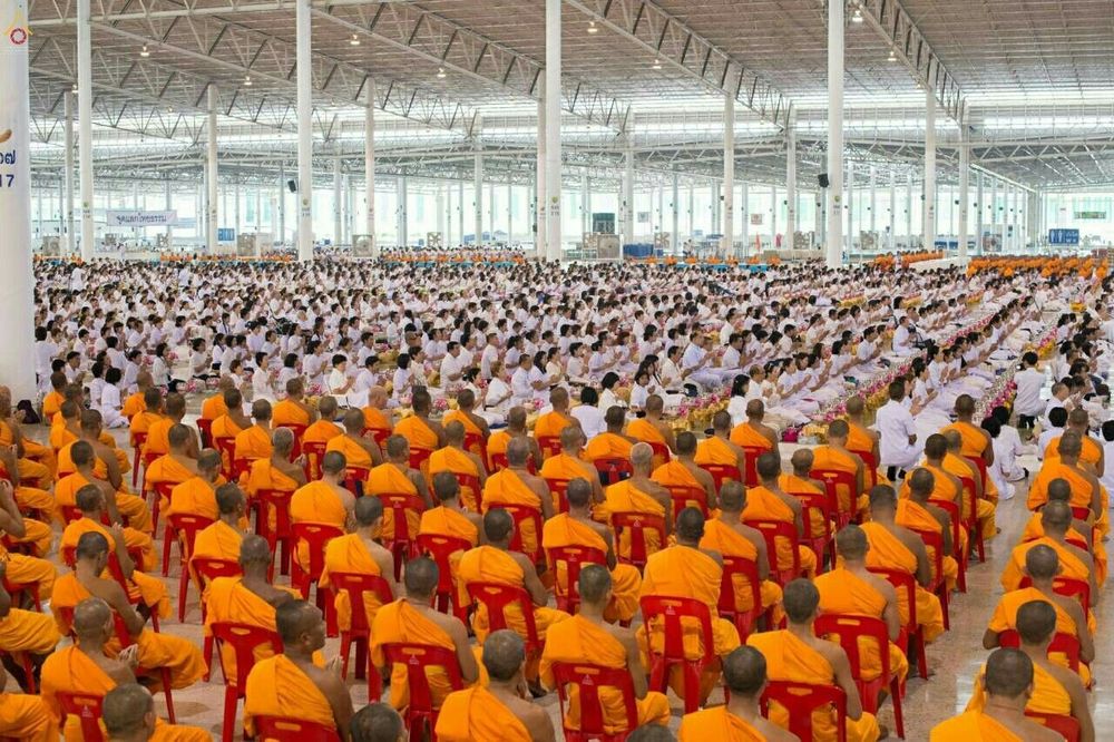 พระภิกษุและพุทธศาสนิกชนจำนวนมากนั่งเรียงรายในอาคารขนาดใหญ่เพื่อร่วมพิธีถวายโคมมาฆประทีป