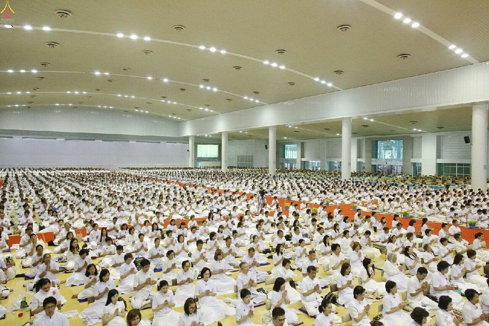 พุทธศาสนิกชนจำนวนมากแต่งกายด้วยชุดสีขาวนั่งพนมมือปฏิบัติธรรมภายในอาคารขนาดใหญ่ในวันสมาธิโลก