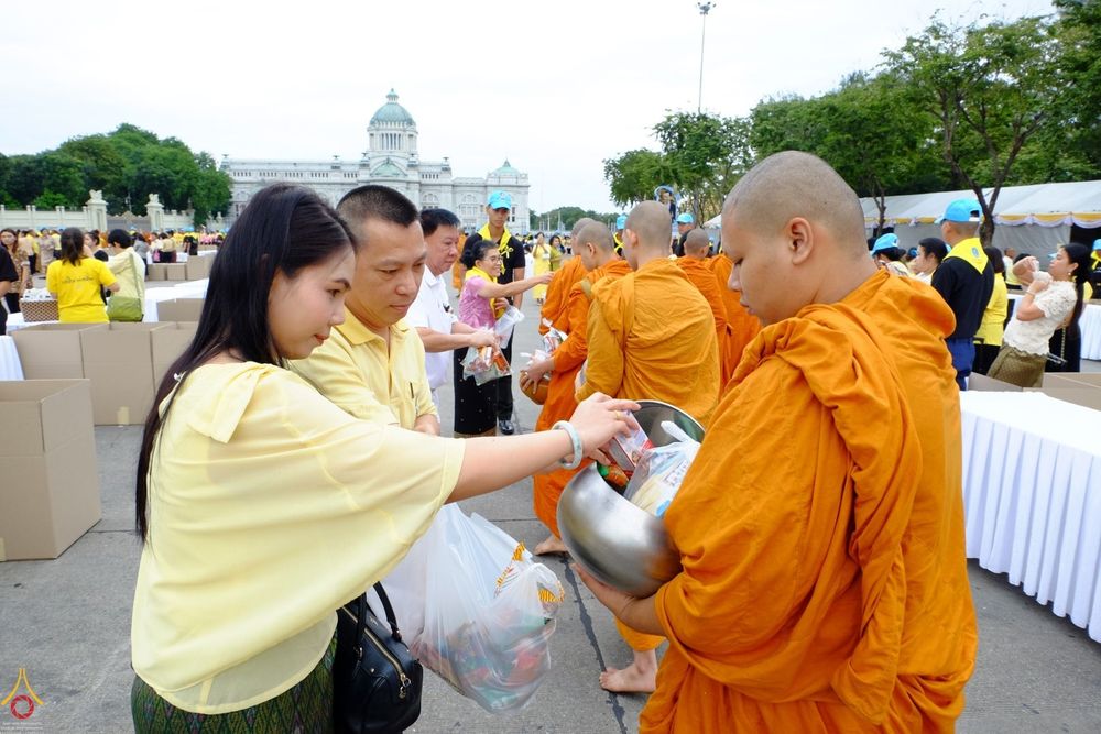 ประชาชนสวมเสื้อสีเหลืองกำลังใส่บาตรพระสงฆ์ในพิธีทำบุญตักบาตร ณ พระลานพระราชวังดุสิต