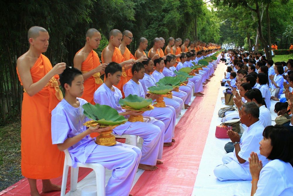 พระสงฆ์ตัดปอยผมให้เยาวชนชายในชุดสีขาวเพื่อเตรียมบรรพชาสามเณร โดยมีญาติโยมนั่งพนมมืออยู่ด้านข้าง