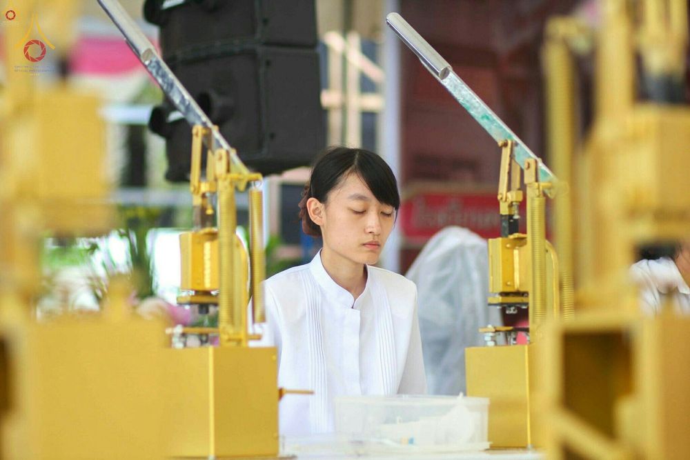 หญิงสาวสวมชุดขาวปฏิบัติธรรมกำลังตั้งใจทำสมาธิในระหว่างการเข้าร่วมพิธีพิมพ์พระของขวัญ รุ่นบรรลุธรรม