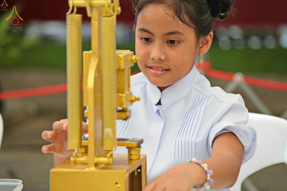 เด็กหญิงสวมชุดสีขาวกำลังใช้เครื่องมือพิมพ์พระของขวัญด้วยความตั้งใจในพิธีทางศาสนา