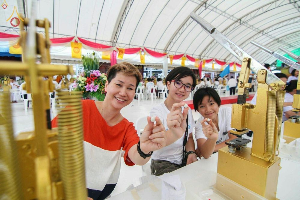 กลุ่มพุทธศาสนิกชนหญิงสามคนกำลังถือองค์พระขนาดเล็กที่พิมพ์เสร็จแล้วในพิธีพิมพ์พระของขวัญรุ่นบรรลุธรรม