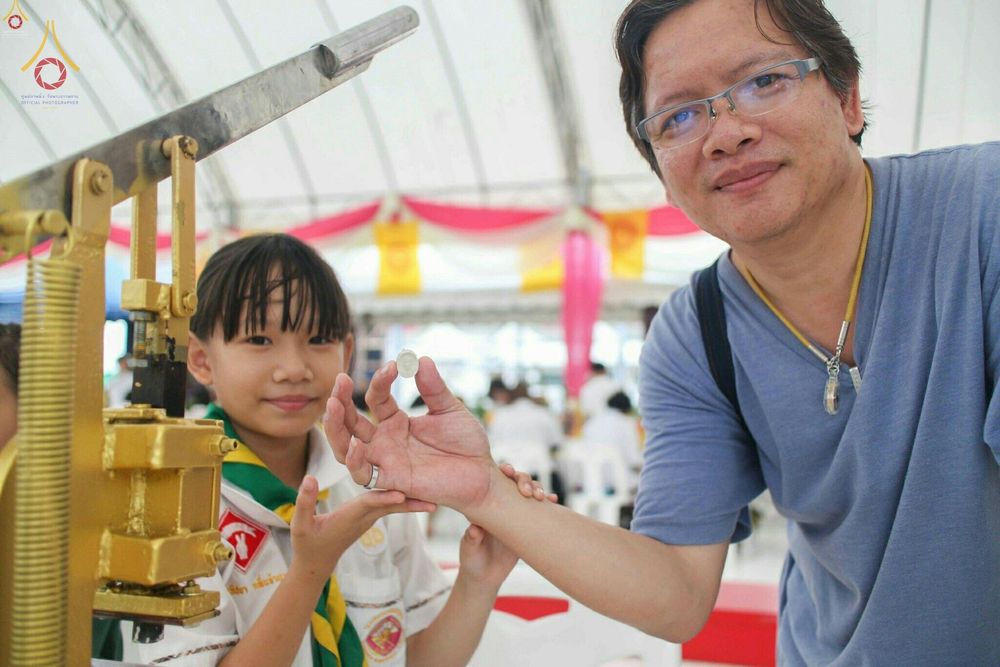 เด็กหญิงในชุดลูกเสือและชายสวมแว่นตากำลังถือพระของขวัญขนาดเล็กที่พิมพ์จากเครื่องกดในพิธี