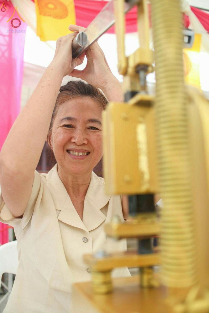 หญิงไทยกำลังใช้เครื่องมือกดพิมพ์พระของขวัญรุ่นบรรลุธรรมด้วยใบหน้ายิ้มแย้ม