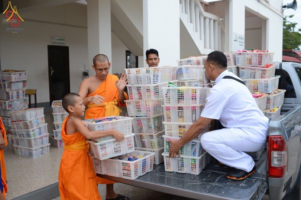 พระสงฆ์ สามเณร และเจ้าหน้าที่ช่วยกันขนตะกร้าสิ่งของตักบาตรลงจากรถกระบะ