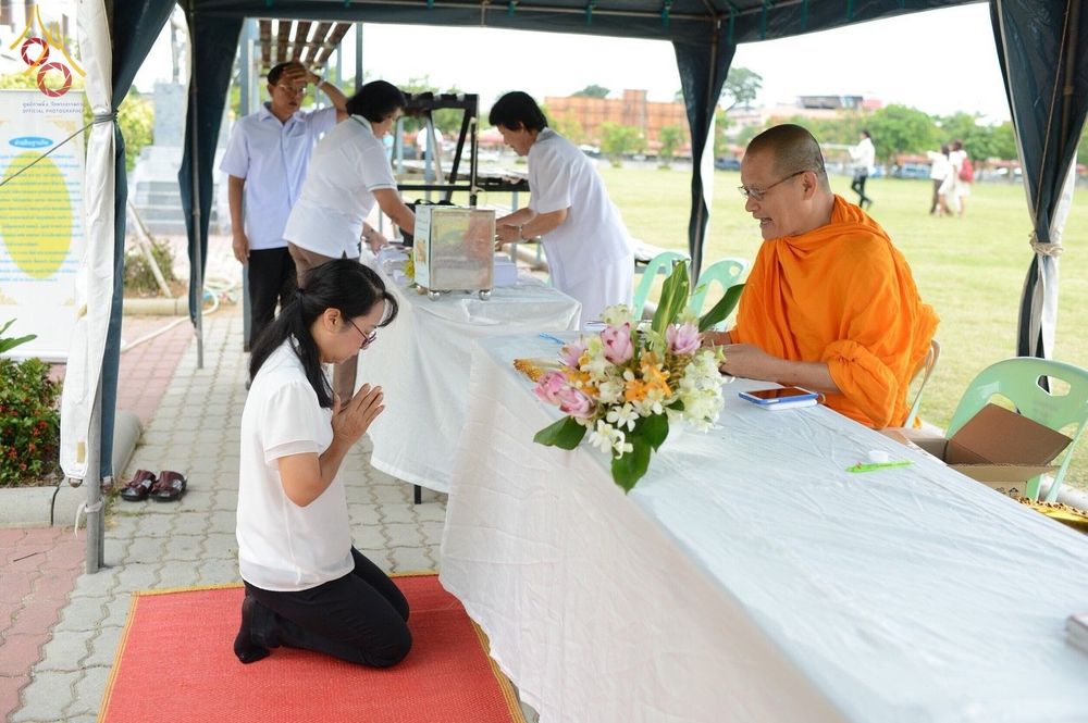 พุทธศาสนิกชนหญิงคุกเข่ากราบพระสงฆ์ที่นั่งประจำจุดรับลงทะเบียนในพิธีตักบาตรคณะสงฆ์ 4 จังหวัดชายแดนภาคใต้