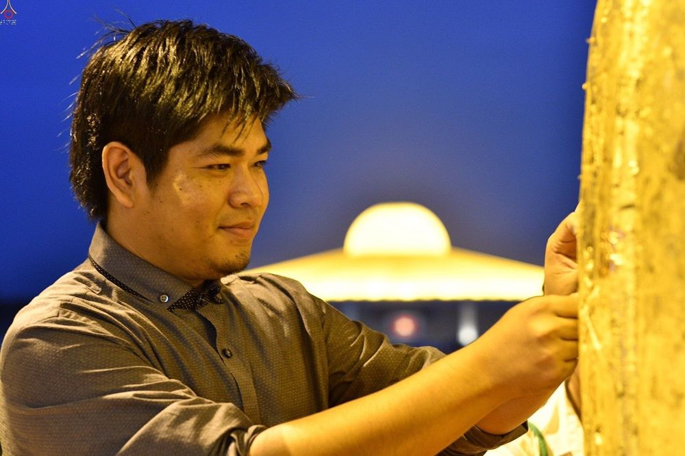 ชายหนุ่มกำลังปิดแผ่นทองบนระฆังธรรมในพิธีกรรมทางศาสนาช่วงเวลากลางคืน