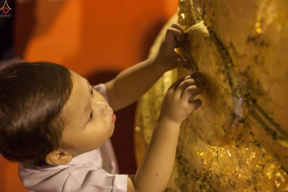 เด็กชายตัวน้อยกำลังปิดแผ่นทองคำเปลวบนระฆังธรรมขนาดใหญ่ด้วยความตั้งใจ