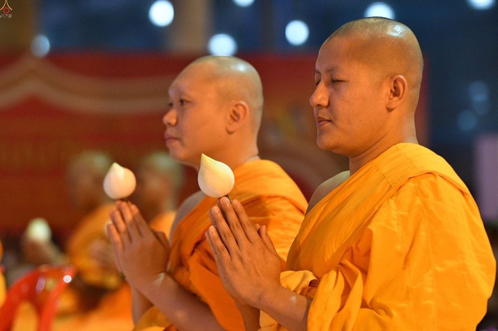 พระภิกษุสงฆ์สองรูปพนมมือถือดอกบัวสีขาวขณะสวดมนต์ในพิธีทางศาสนา