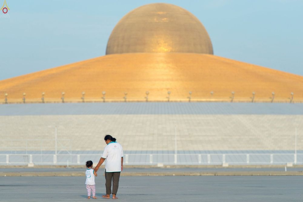 หญิงวัยกลางคนจูงมือเด็กหญิงเดินหน้ามหาธรรมกายเจดีย์สีทองขนาดใหญ่