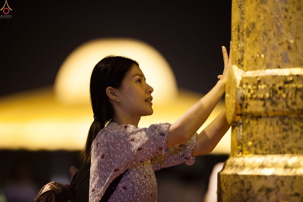 หญิงสาวกำลังปิดแผ่นทองบนระฆังธรรมในพิธีทางศาสนาช่วงเวลากลางคืน