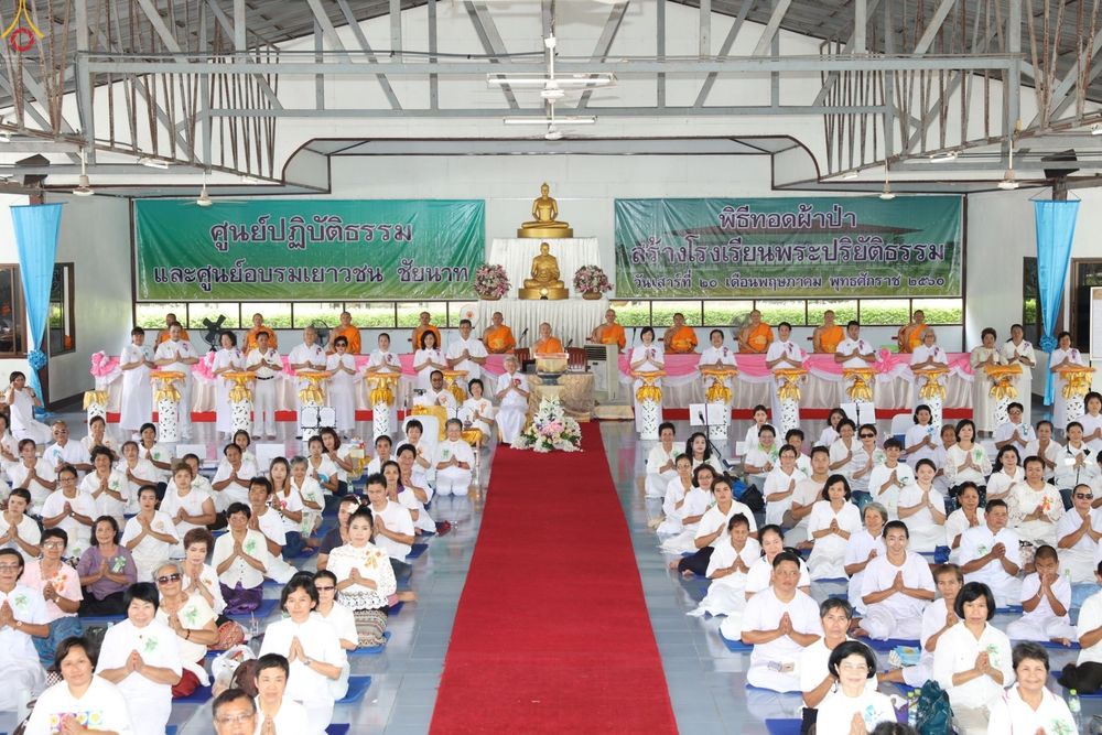 พุทธศาสนิกชนสวมชุดขาวนั่งพนมมือร่วมพิธีทอดผ้าป่าสร้างโรงเรียนพระปริยัติธรรมภายในอาคารศูนย์ปฏิบัติธรรมและศูนย์อบรมเยาวชน จังหวัดชัยนาท