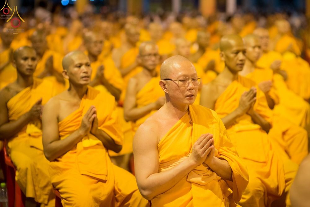 พระภิกษุสงฆ์จำนวนมากกำลังนั่งพนมมือสวดมนต์ในพิธีสวดธัมมจักกัปปวัตนสูตรที่วัดพระธรรมกาย