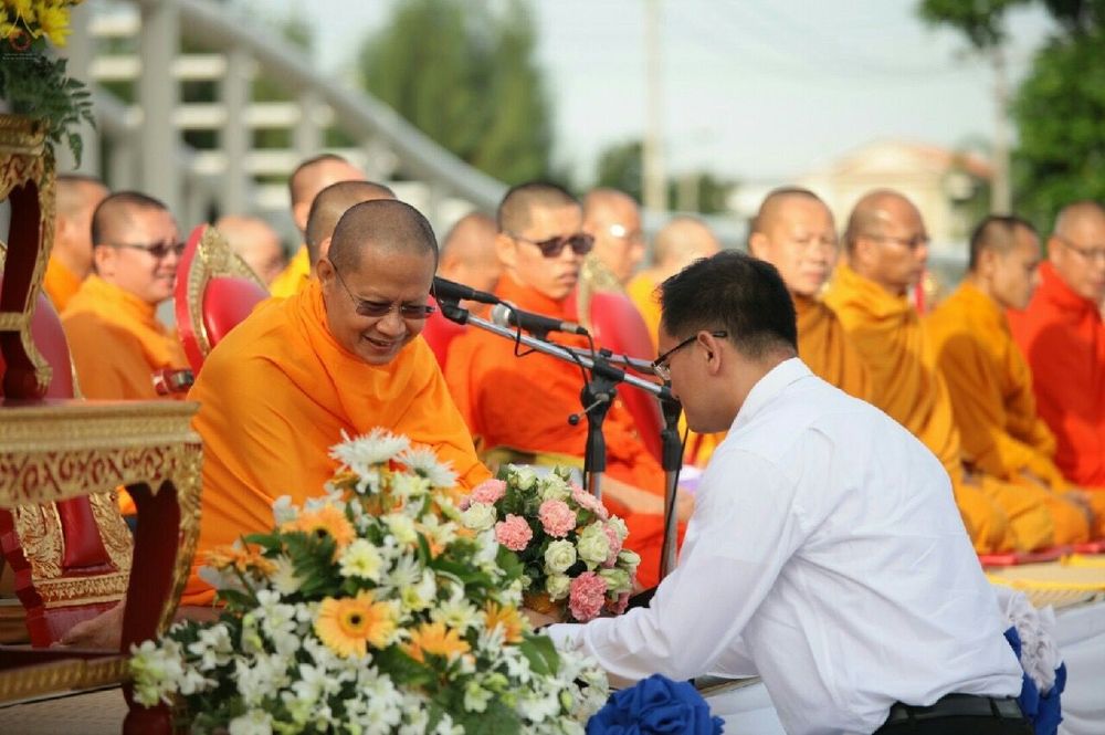 ชายสวมเสื้อเชิ้ตสีขาวกำลังถวายเครื่องสักการะแด่พระภิกษุสงฆ์ในงานตักบาตรกตัญญู