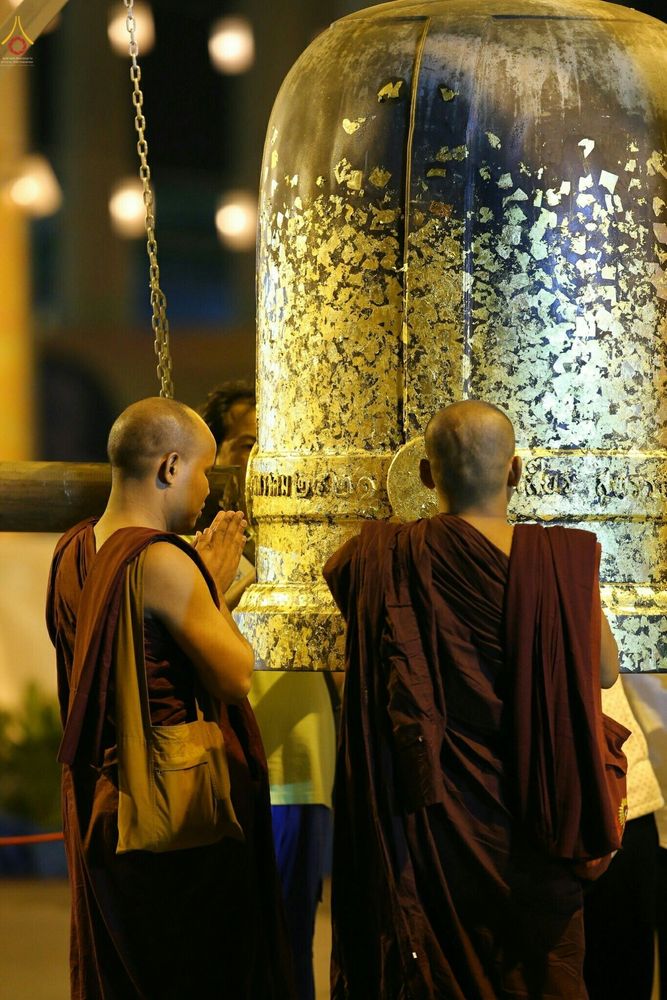 พระสงฆ์สองรูปยืนพนมมือหน้าไประฆังใบใหญ่ที่ปิดทองคำเปลวในพิธีกรรมทางศาสนา