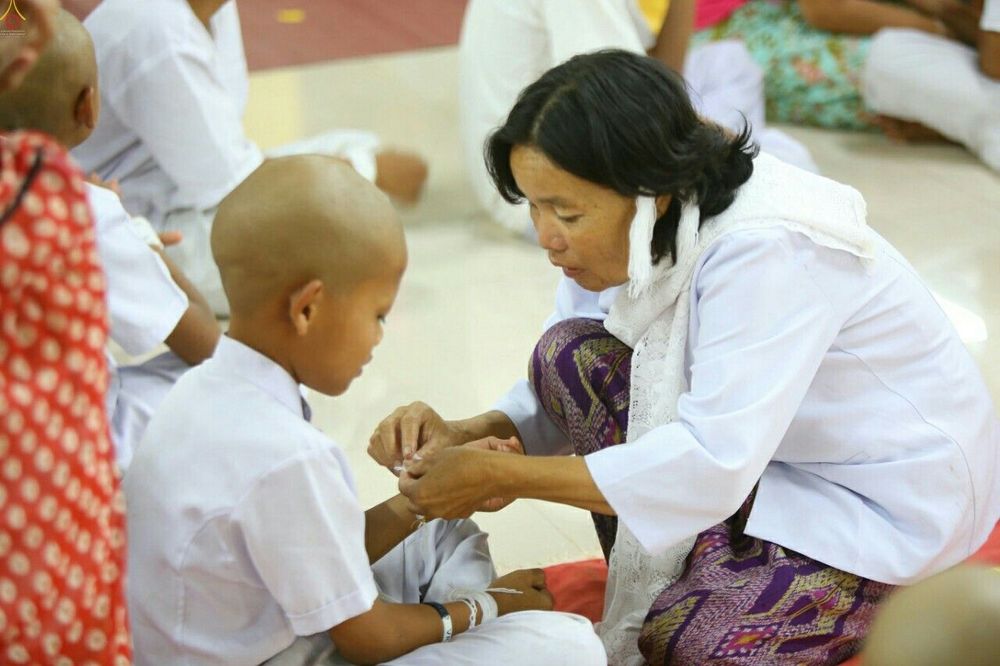 หญิงไทยกำลังผูกข้อมือให้เด็กชายที่โกนผมเตรียมบวชในพิธีทำขวัญนาค