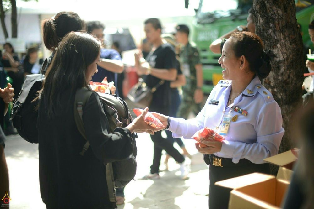 เจ้าหน้าที่ในเครื่องแบบกำลังยื่นถุงอาหารและน้ำดื่มให้กับประชาชนที่มาสักการะพระบรมศพฯ