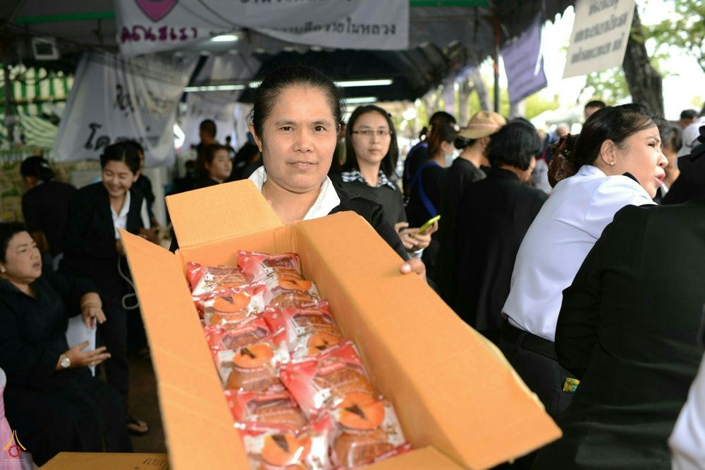 หญิงไทยถือกล่องขนมปังแจกจ่ายให้ประชาชนที่มาสักการะพระบรมศพ