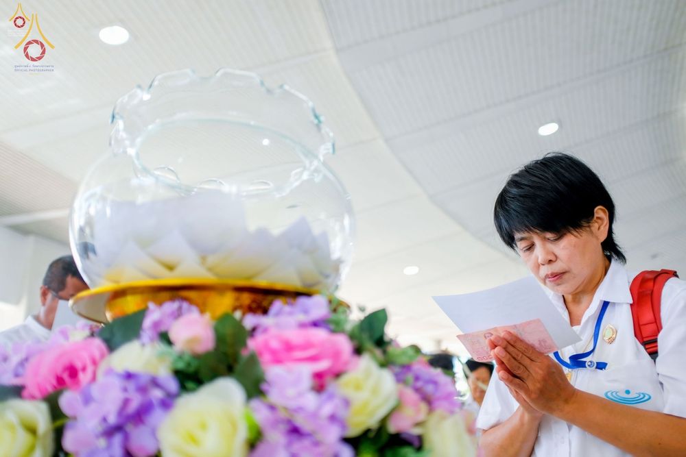 หญิงชาวพุทธสวมชุดขาวถือรายชื่ออธิษฐานจิตในพิธีบุพเปตพลี ณ วัดพระธรรมกาย