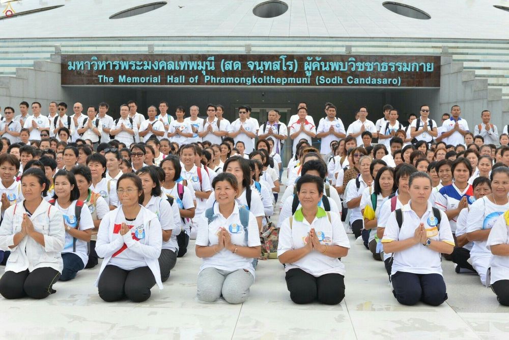 กลุ่มพุทธศาสนิกชนนั่งพนมมือหน้ามหาวิหารพระมงคลเทพมุนี วัดพระธรรมกาย