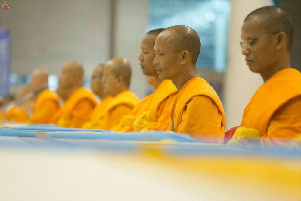 พระภิกษุสงฆ์ห่มจีวรสีเหลืองทองกำลังนั่งหลับตาทำสมาธิเรียงแถวกันอย่างเป็นระเบียบในพิธีทางศาสนา