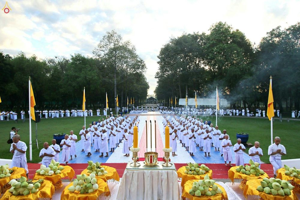 กลุ่มนาคธรรมทายาทสวมชุดขาวพนมมือประกอบพิธีทางศาสนากลางแจ้ง มีพานดอกบัววางเรียงรายอยู่ด้านหน้า