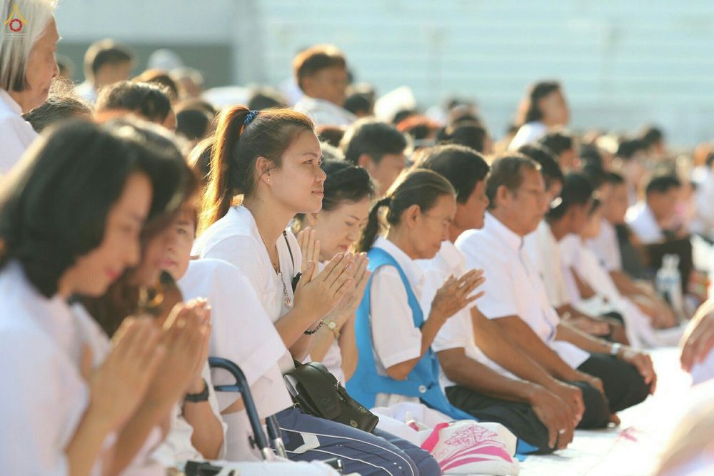 กลุ่มพุทธศาสนิกชนแต่งกายด้วยชุดสีขาวนั่งพนมมือด้วยความสงบในพิธีบรรพชาอุปสมบทหมู่นาคธรรมทายาท
