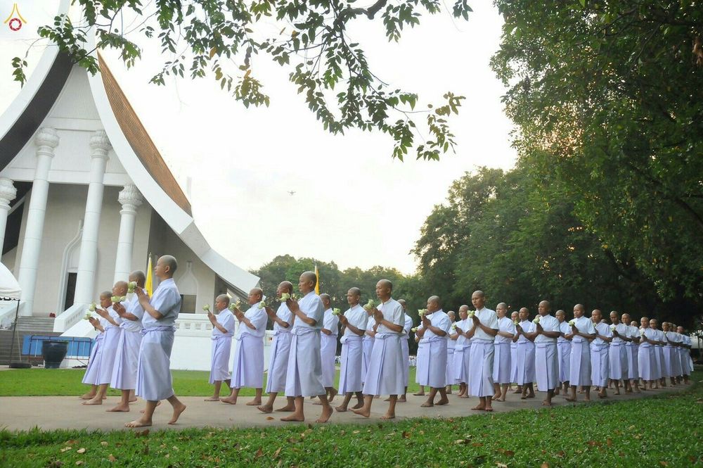 กลุ่มนาคธรรมทายาทในชุดขาวถือดอกบัวเดินแถวเข้าสู่พิธีบรรพชาอุปสมบทหมู่หน้าอาคารศาสนสถาน