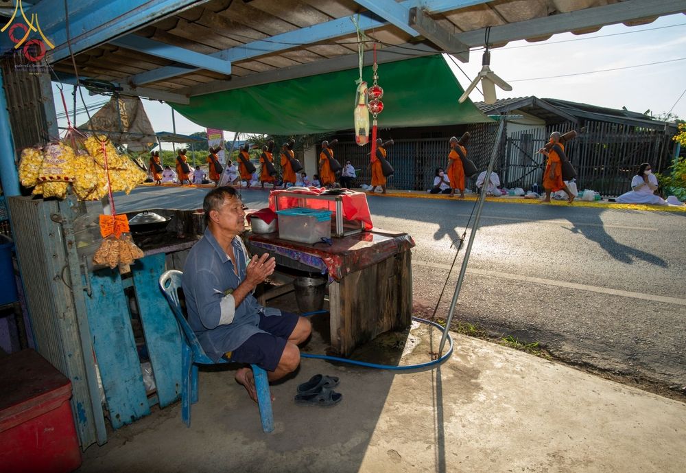 ชายไทยนั่งพนมมือต้อนรับคณะพระภิกษุสงฆ์ที่กำลังเดินธุดงค์ผ่านเส้นทางบริเวณวัดบางปลา