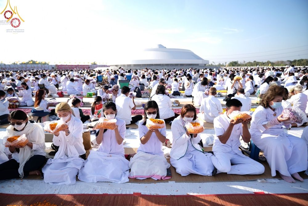 พุทธศาสนิกชนในชุดขาวถือถุงดอกดาวเรืองร่วมพิธีต้อนรับพระธรรมยาตรา ณ อนุสรณ์สถานบางปลา