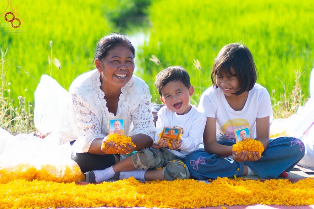 หญิงสูงวัยและเด็กสองคนถือภาพพระมงคลเทพมุนีและโปรยกลีบดอกดาวเรืองสีเหลืองเพื่อต้อนรับคณะพระธรรมยาตรา