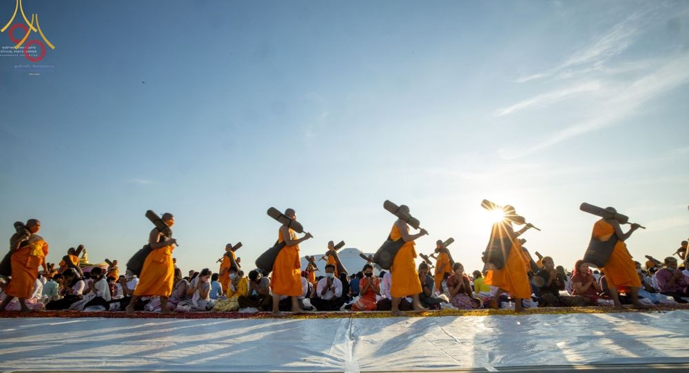 คณะพระธรรมยาตราเดินธุดงค์สะพายกลดท่ามกลางพุทธศาสนิกชนที่นั่งรอต้อนรับในยามเย็น