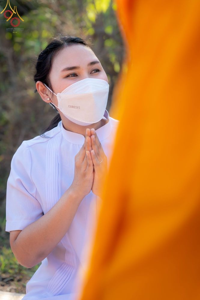 หญิงสาวสวมชุดขาวประนมมือไหว้พระภิกษุสงฆ์ในพิธีต้อนรับพระธรรมยาตรา